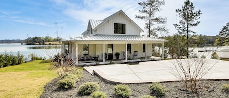 A white house with a covered porch, a large driveway, and a lake view.