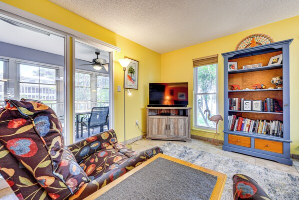 A living room with a sofa, a bookshelf, a television, and a window with a view of the outside. - St Johns River Retreat in Welaka w/ Dock Access (Welaka)