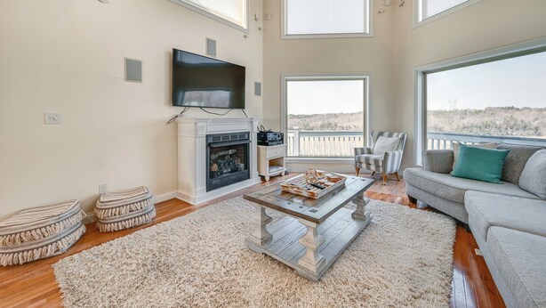 A spacious living room with a fireplace, a television, and a large window offering a view of the landscape. - Lake Cumberland Home w/ Hot Tub & Game Room (Bronston)