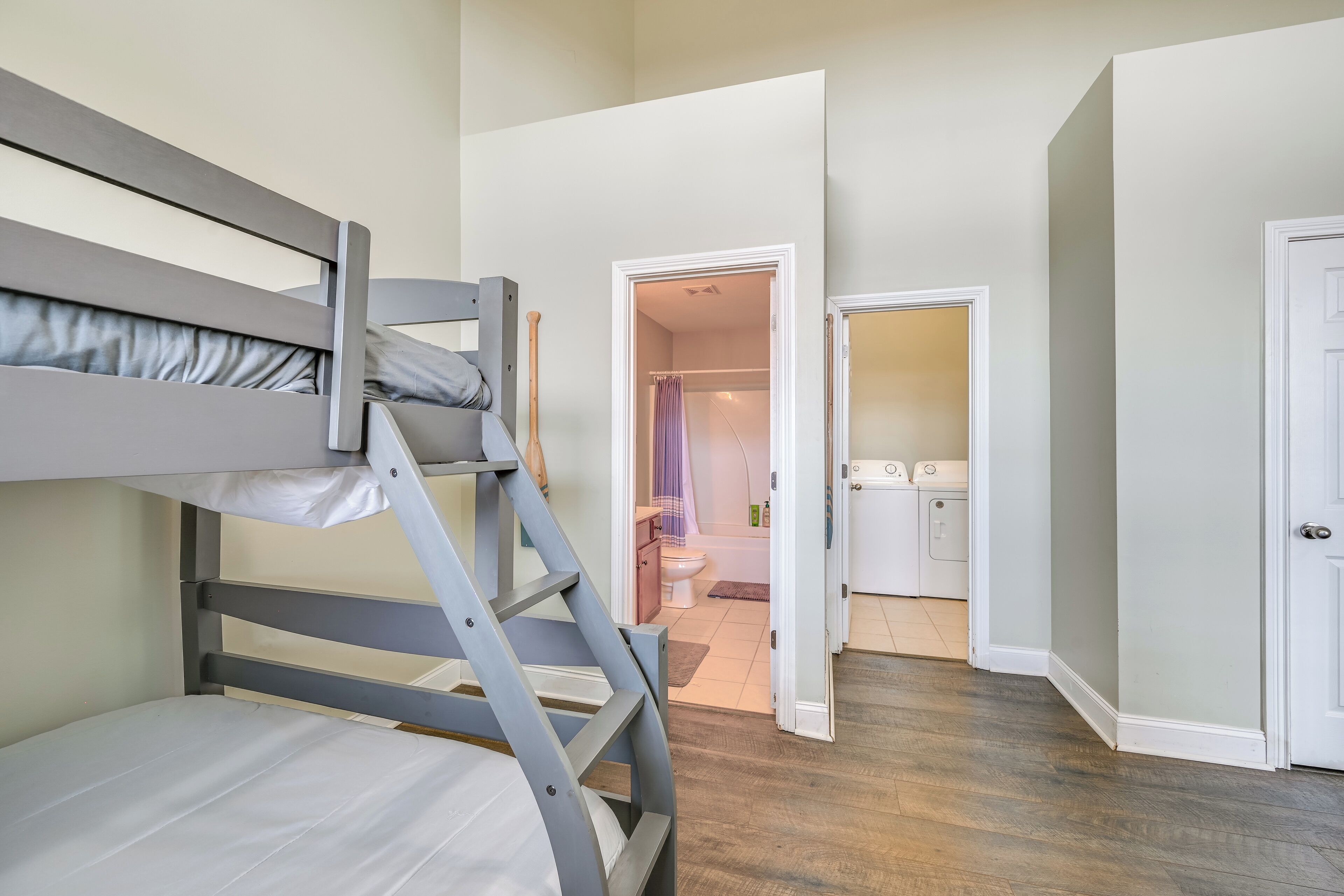 A bunk bed in a room with a wooden floor and white walls. There is a bathroom visible through an open door.