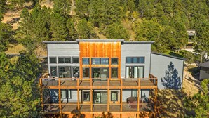 Ein modernes mehrgeschossiges Haus mit einer Holzterrasse und großen Fenstern, umgeben von Bäumen.