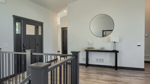 Ein modernes Interieur mit Treppe, einer dunklen Tür, einem runden Spiegel und einem kleinen Konsolentisch mit Lampe.