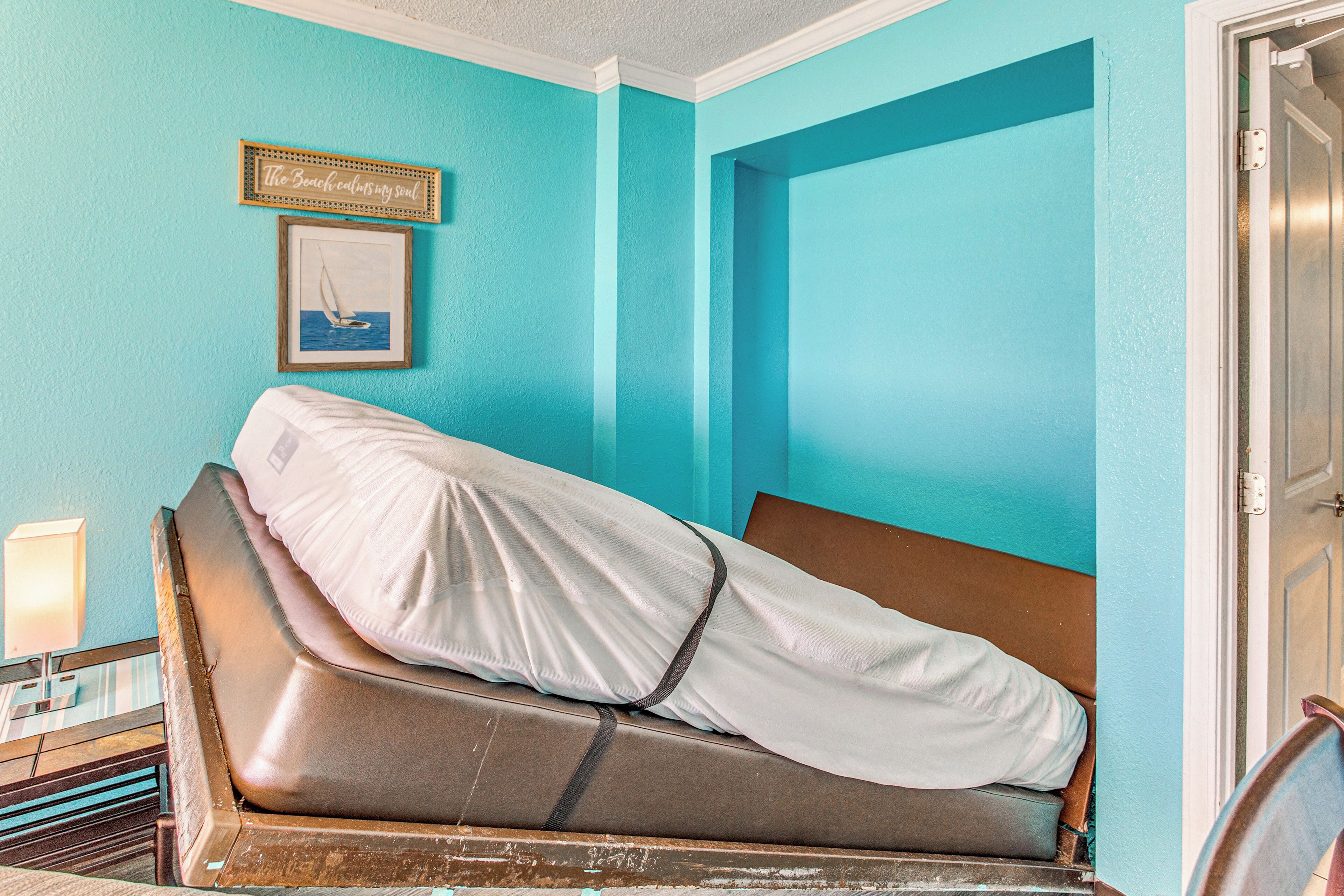 A room with teal walls, a bed with a white cover, a framed picture, and a door.