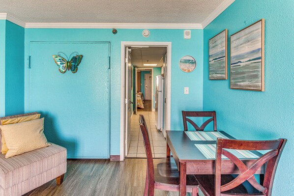A room with a dining table, chairs, a sofa, and a door with a butterfly decoration. - Sun, Sand & Sea Views: Myrtle Beach Condo (Myrtle Beach)