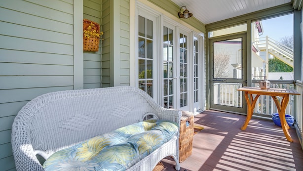 A wicker sofa with a floral cushion on a covered porch with a wooden table and chairs. - Walk to Beach: Cape May Home w/ Screened Patio! (Cape May)