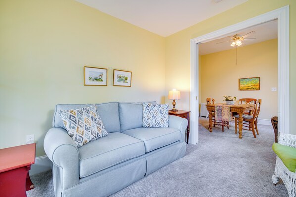 A living room with a light blue sofa, a red side table, a dining area with a wooden table and chairs, and a ceiling fan. - Walk to Beach: Cape May Home w/ Screened Patio! (Cape May)