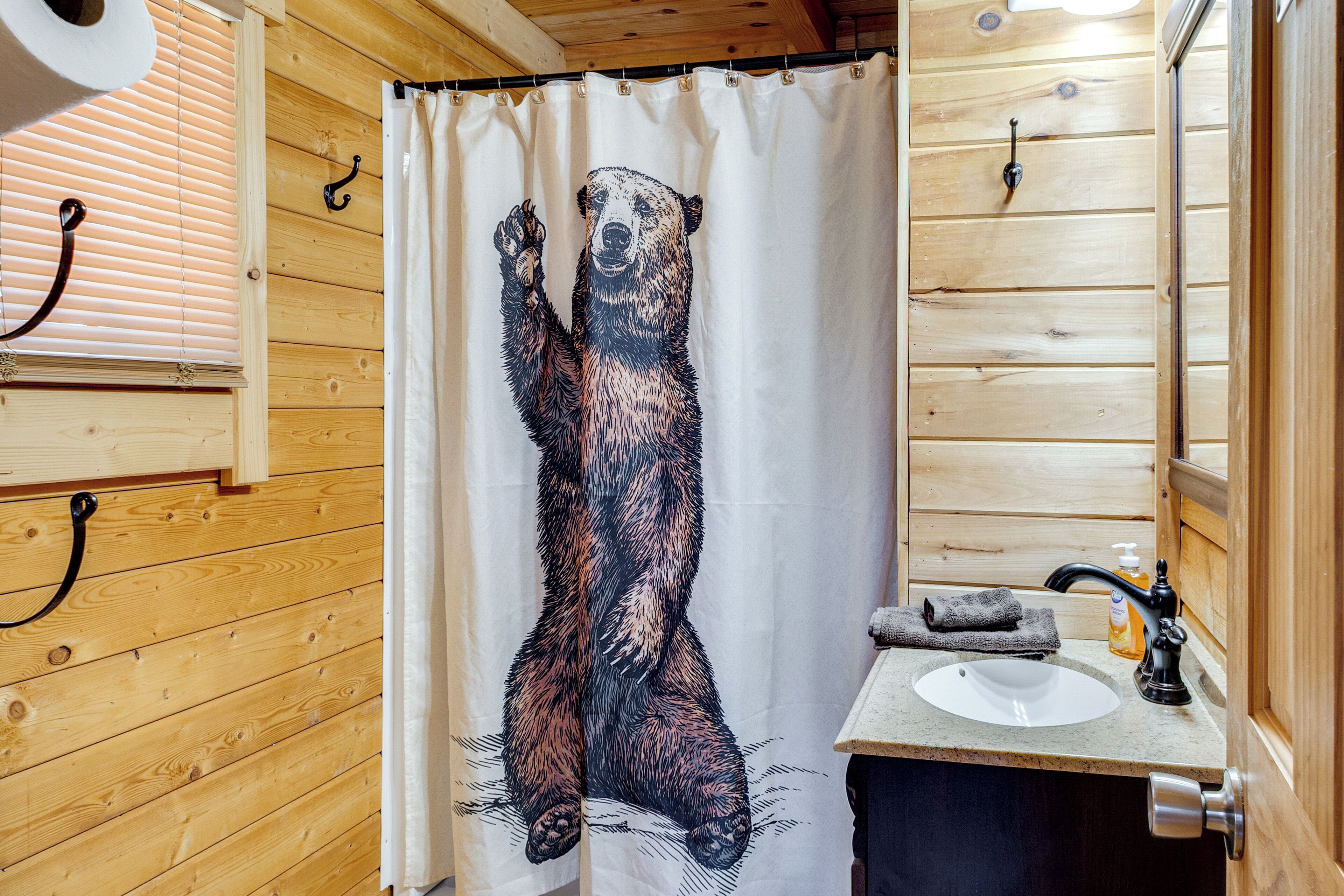 A bathroom with a wooden interior, a bear-themed shower curtain, a sink with a soap dispenser, and a towel hanging on the wall.