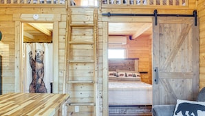 A wooden cabin interior with a bed, a wooden table, and a bear sculpture. - Fire Pit + Pool Access: Cozy Cabin in Sevierville! (Sevierville)