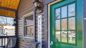 A log cabin with a green door, a welcome sign, and a bench outside. - Fire Pit + Pool Access: Cozy Cabin in Sevierville! (Sevierville)