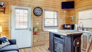 A cozy cabin interior with a wooden interior, a kitchen area with a microwave, and a door with a fire extinguisher. - Fire Pit + Pool Access: Cozy Cabin in Sevierville! (Sevierville)