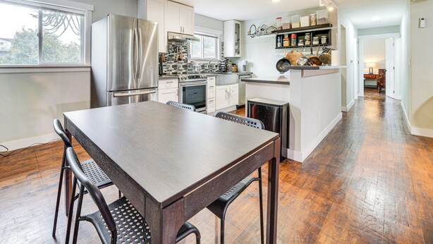 Une cuisine moderne dotée d’appareils électroménagers en acier inoxydable, un coin repas avec une table et des chaises en bois, et une vue sur l’extérieur grâce à une grande fenêtre.