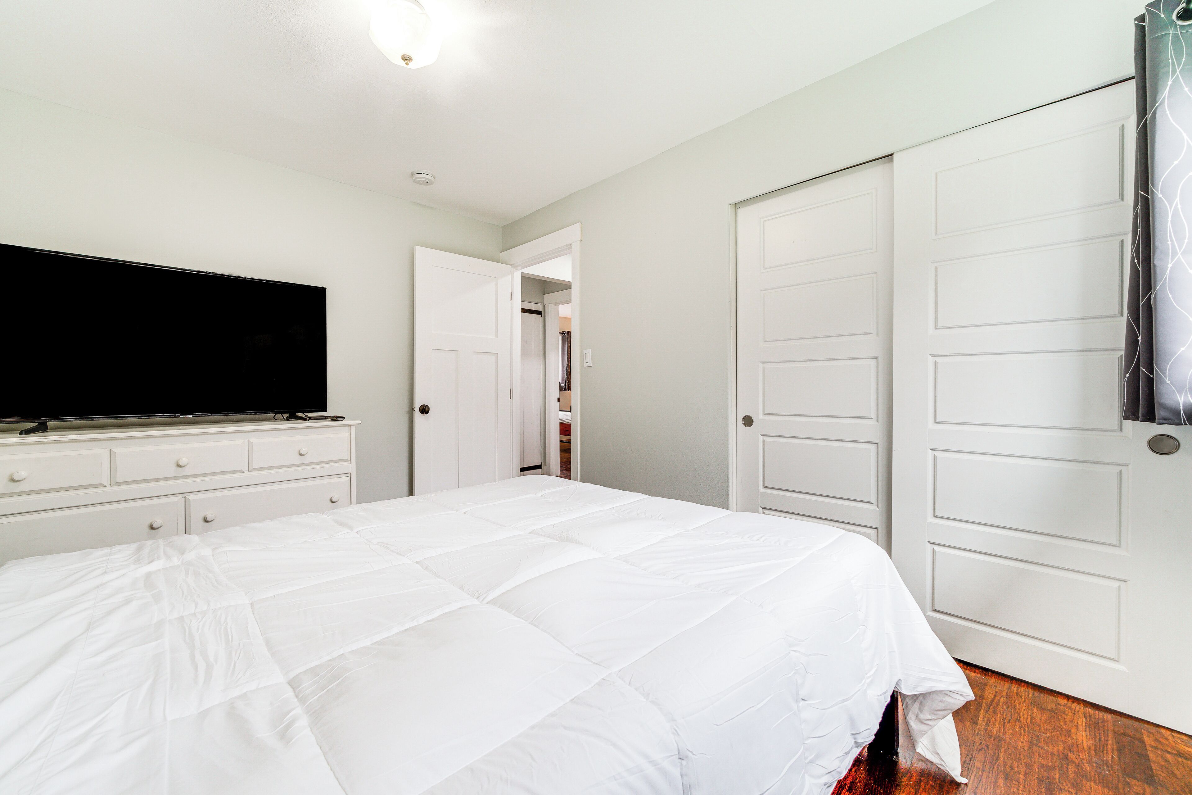 A bedroom with a large bed, a TV on a dresser, and white doors.