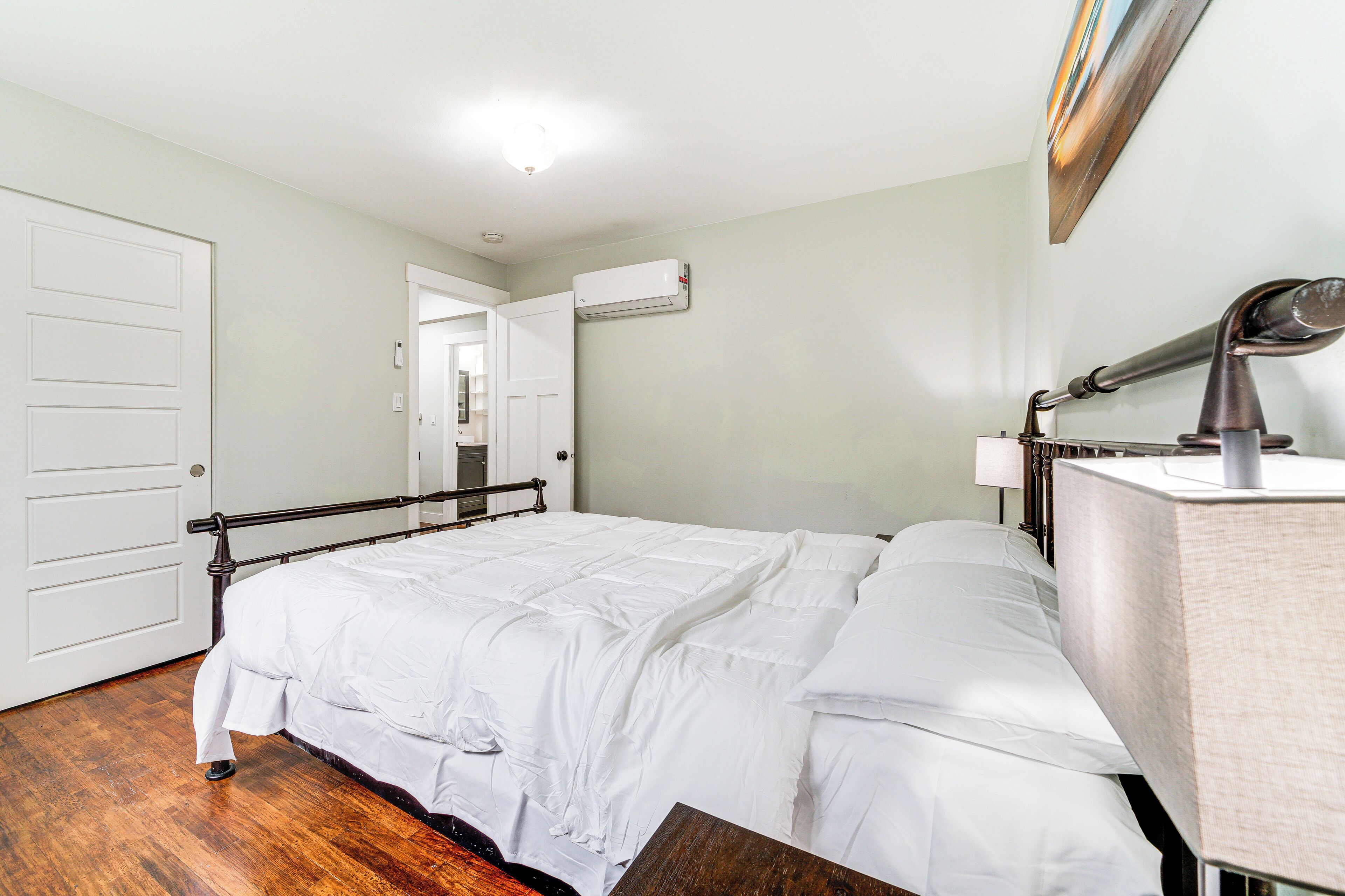 A neatly made bed with white linens, a bedside lamp, and a wall-mounted air conditioner.