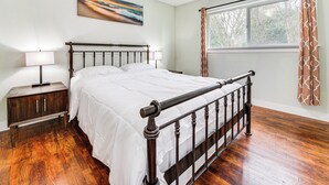 Une chambre à coucher avec un lit en bois, des tables de chevet, une fenêtre avec des rideaux et un tableau au mur.