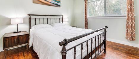 A bedroom with a wooden bed, bedside tables, a window with curtains, and a painting on the wall.