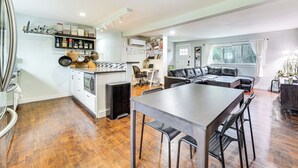 Un vaste espace de vie comprenant un coin repas avec une table, un canapé en cuir noir et une cuisine avec un îlot central en bois.