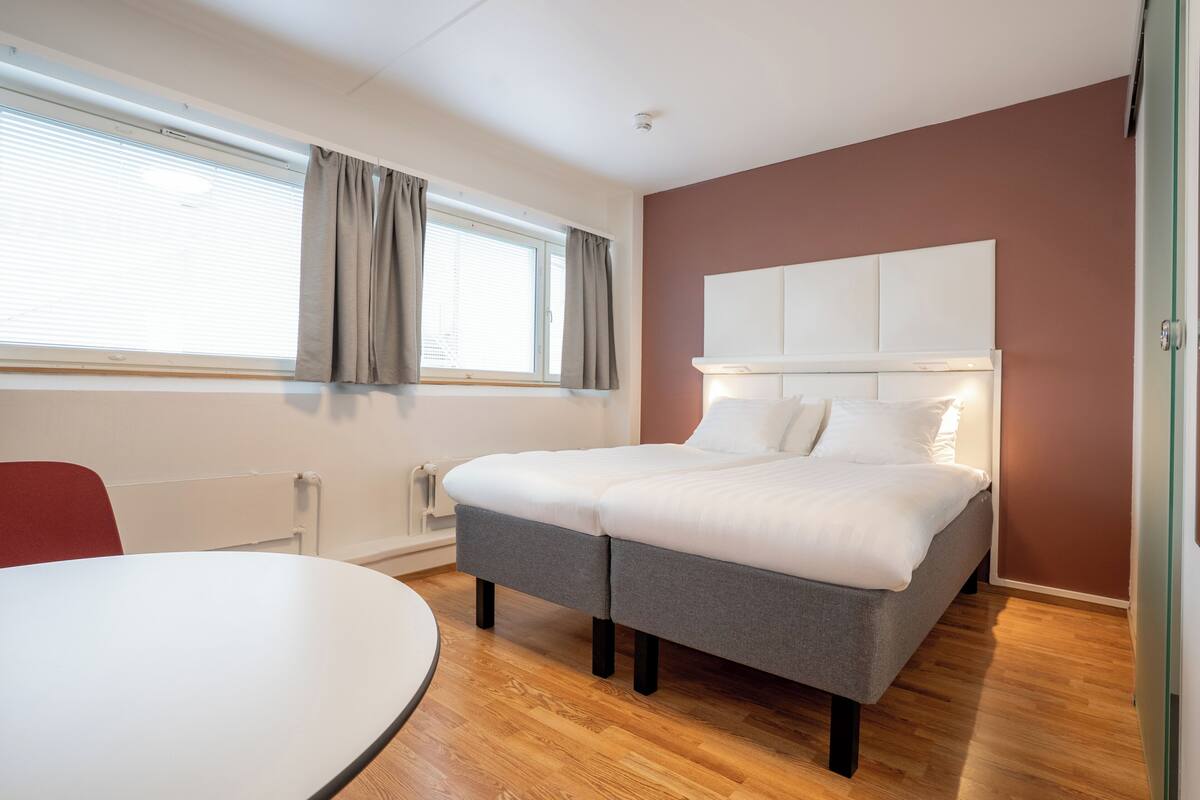 A modern bedroom with a large bed, a bedside table, a round table, and a window with curtains.