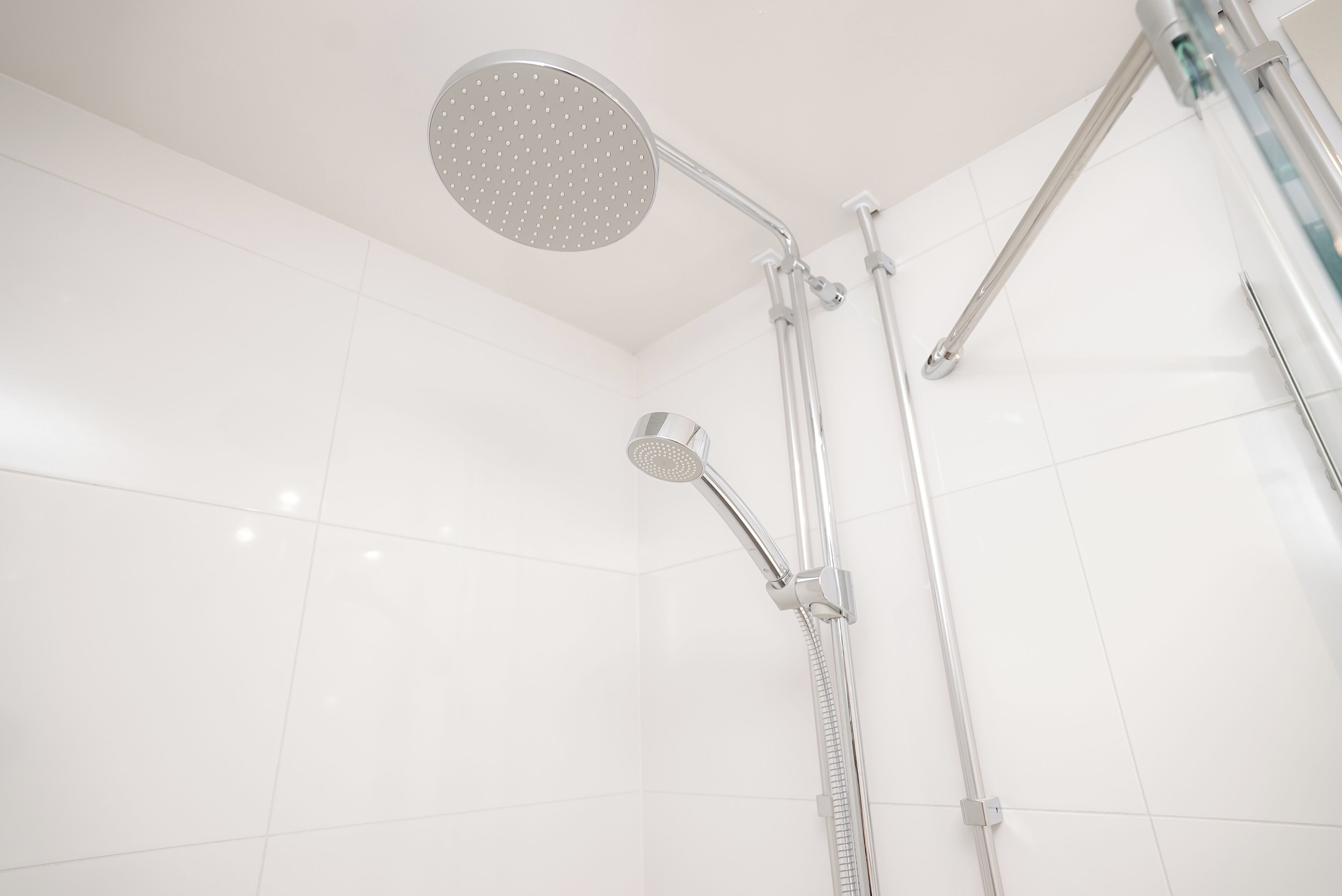 A modern shower with a handheld showerhead and a fixed overhead showerhead, both with chrome finishes.