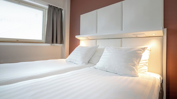 A hotel room with two beds, a large window with curtains, and a headboard with built-in lighting. - Omena Hotel Hanko (Hanko)