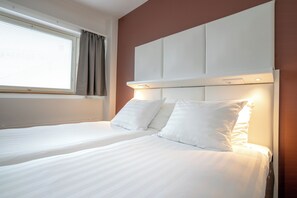 A hotel room with two beds, a large window with curtains, and a headboard with built-in lighting. - Omena Hotel Hanko (Hanko)