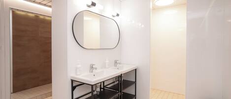 A modern bathroom with two white sinks, a large mirror, and a black shelving unit.