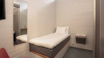 A small, single-bed room with a wooden frame, a white mattress, and a red chair.