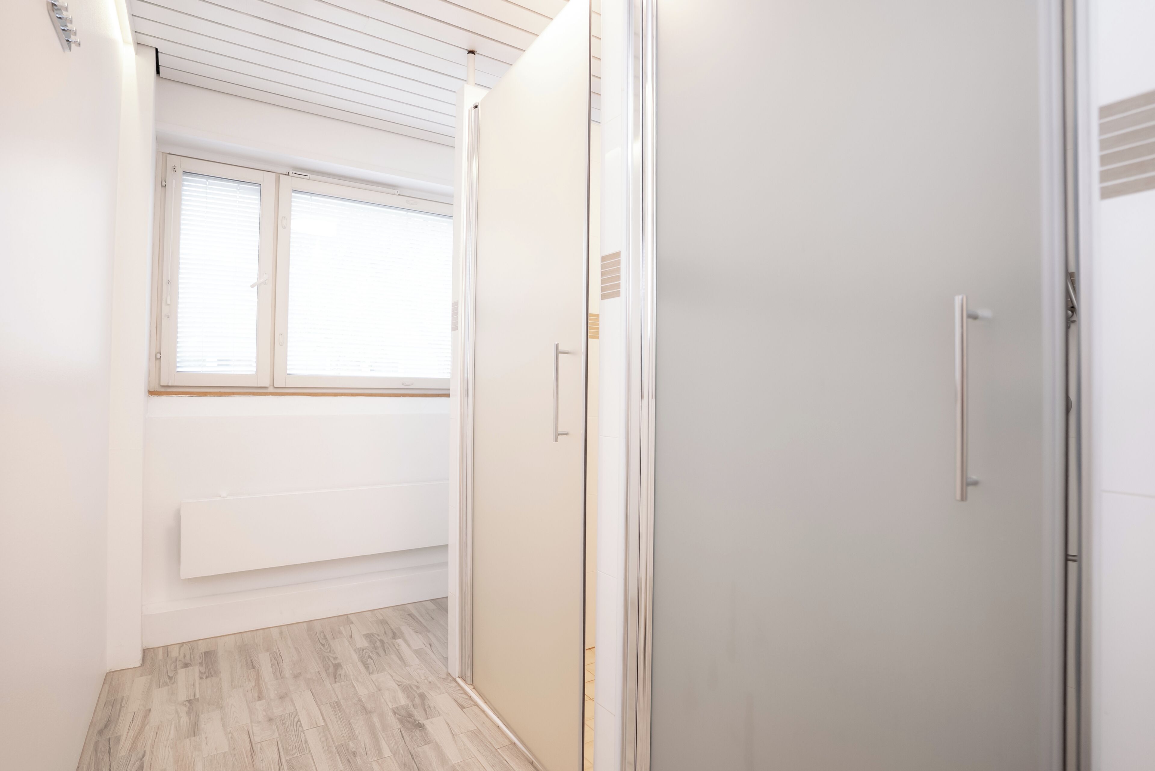 A narrow hallway with a radiator, a sliding glass door, and a window with blinds.