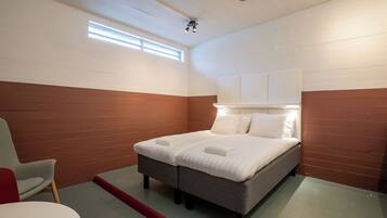 Una cama individual con cabecera, una silla y una mesita de noche en una habitación con paredes blancas y marrones.