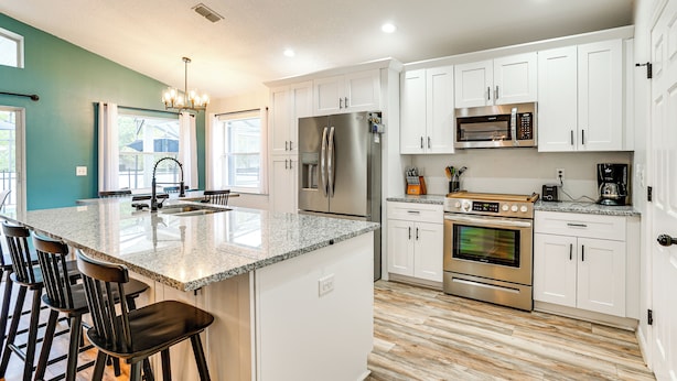 A modern kitchen with white cabinets, stainless steel appliances, a granite countertop, and a bar area with stools.