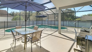 A covered outdoor area with a glass table, chairs, and a pool.