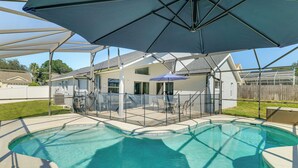 A backyard with a swimming pool, covered patio area, and umbrellas providing shade.