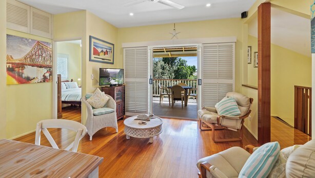 A spacious living room with a wooden floor, a ceiling fan, a television, and a dining area with a table and chairs.