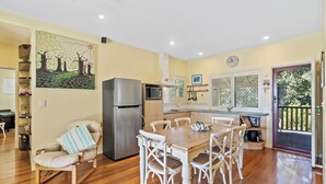 A compact kitchen with a refrigerator, microwave, and dining area with white chairs and a wooden table.