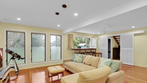 A spacious living room with a large beige sofa, a wooden coffee table, and a telescope on a tripod.