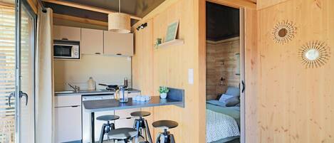 A compact kitchen with a microwave, sink, and stools.