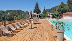 A wooden deck with sun loungers and umbrellas, a swimming pool, and a building in the background. - CityKamp d'Aix en Provence  (Aix-en-Provence)