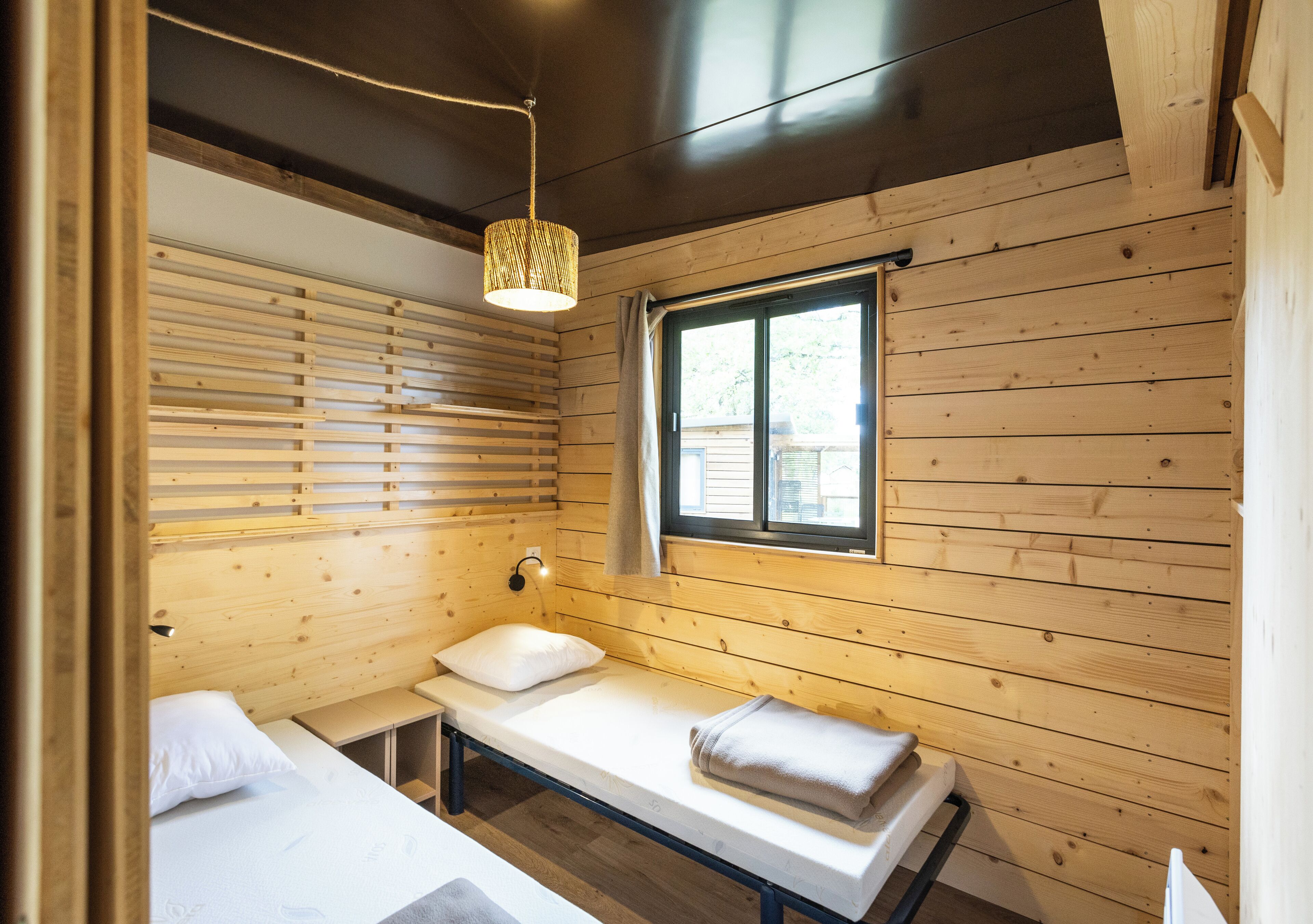 Una habitación de cabaña de madera con cama, un banco, una ventana y una lámpara colgante.