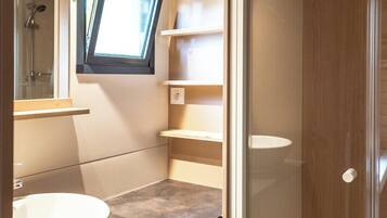 Een kleine badkamer met een groot wit wastafel, een douchecabine en inbouwplanken.