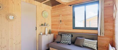 L’intérieur d’un chalet accueillant, avec un mur en bois, un canapé agrémenté de coussins à motifs, une petite table sur laquelle se trouve un bol, et un luminaire suspendu.