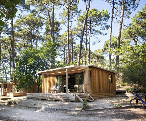 Una cabaña de madera con porche y zona de estar al aire libre, rodeada de árboles.