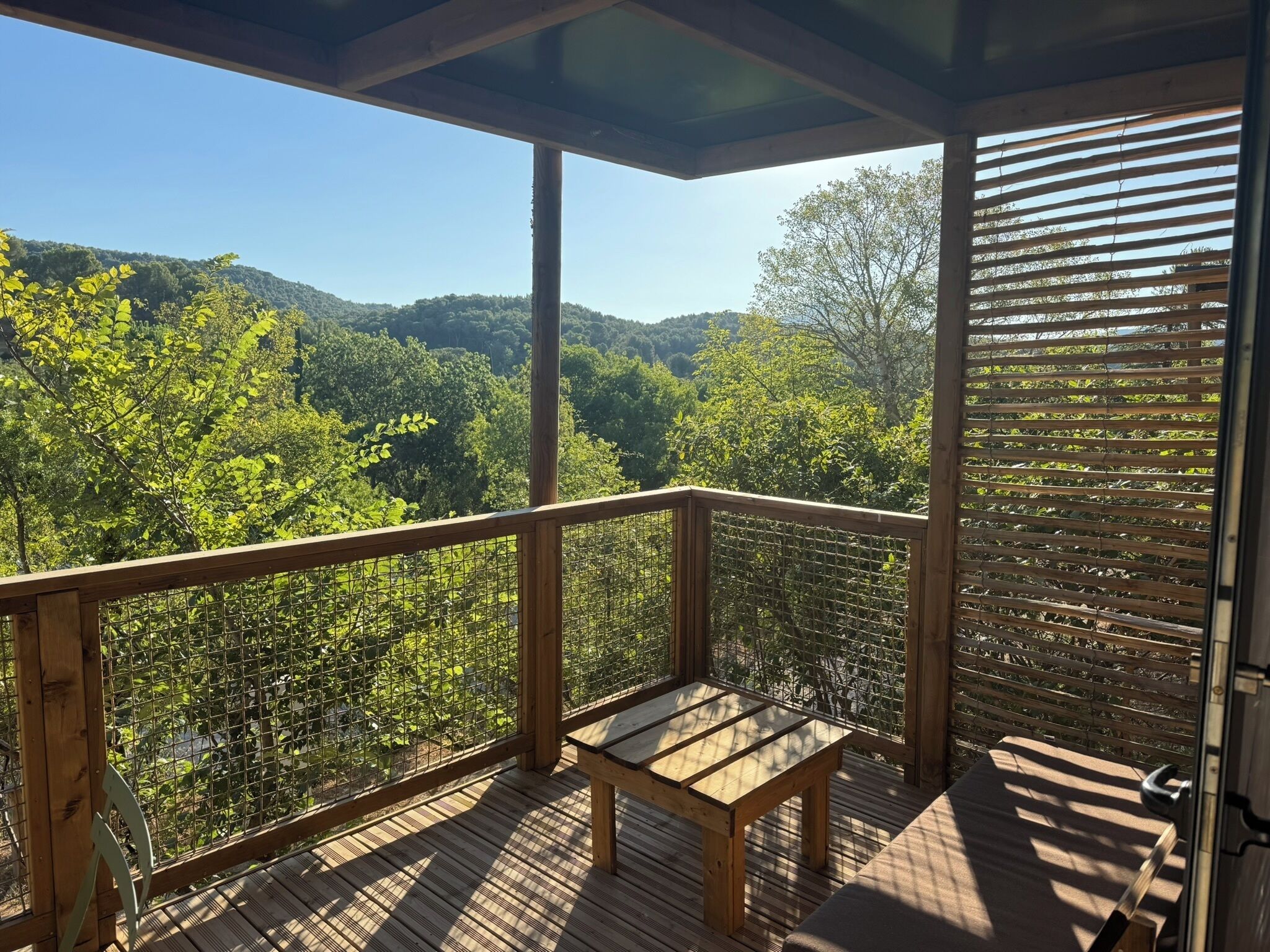 Una terraza de madera con una mesa y un banco, con vistas a un valle boscoso.