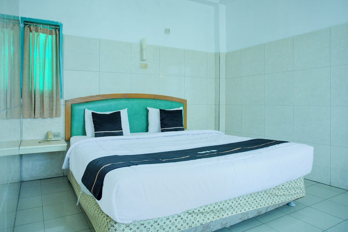A neatly made bed with a patterned bedspread, a headboard, and a bedside table with a telephone.
