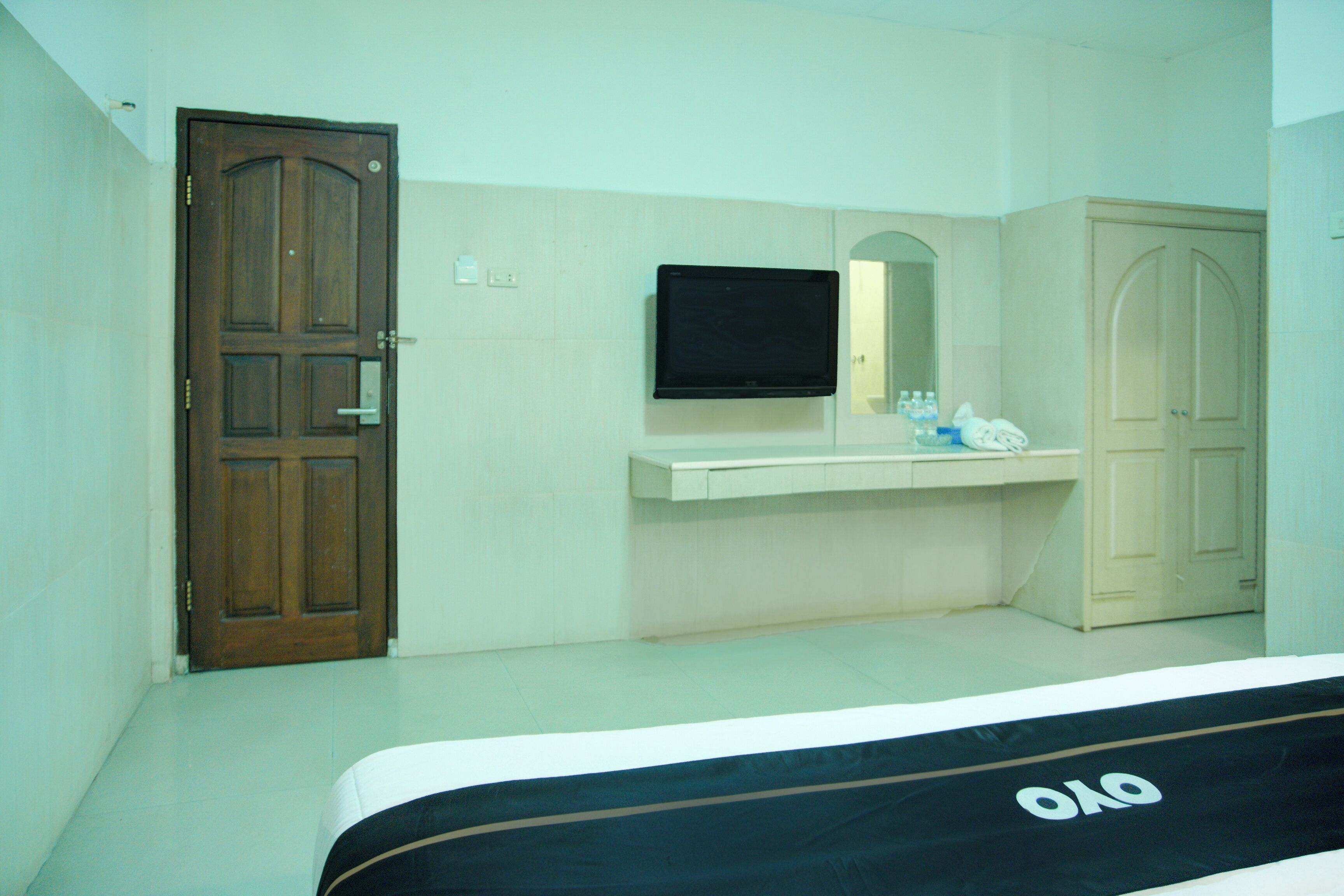 Una habitación de hotel con una puerta de madera, un televisor sobre una encimera blanca y un armario.