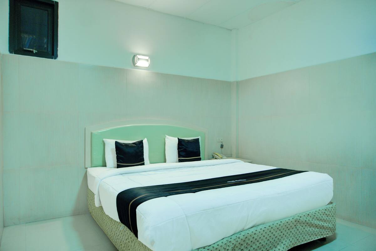 A hotel room with a bed, a nightstand, a wall-mounted light, and a small window.