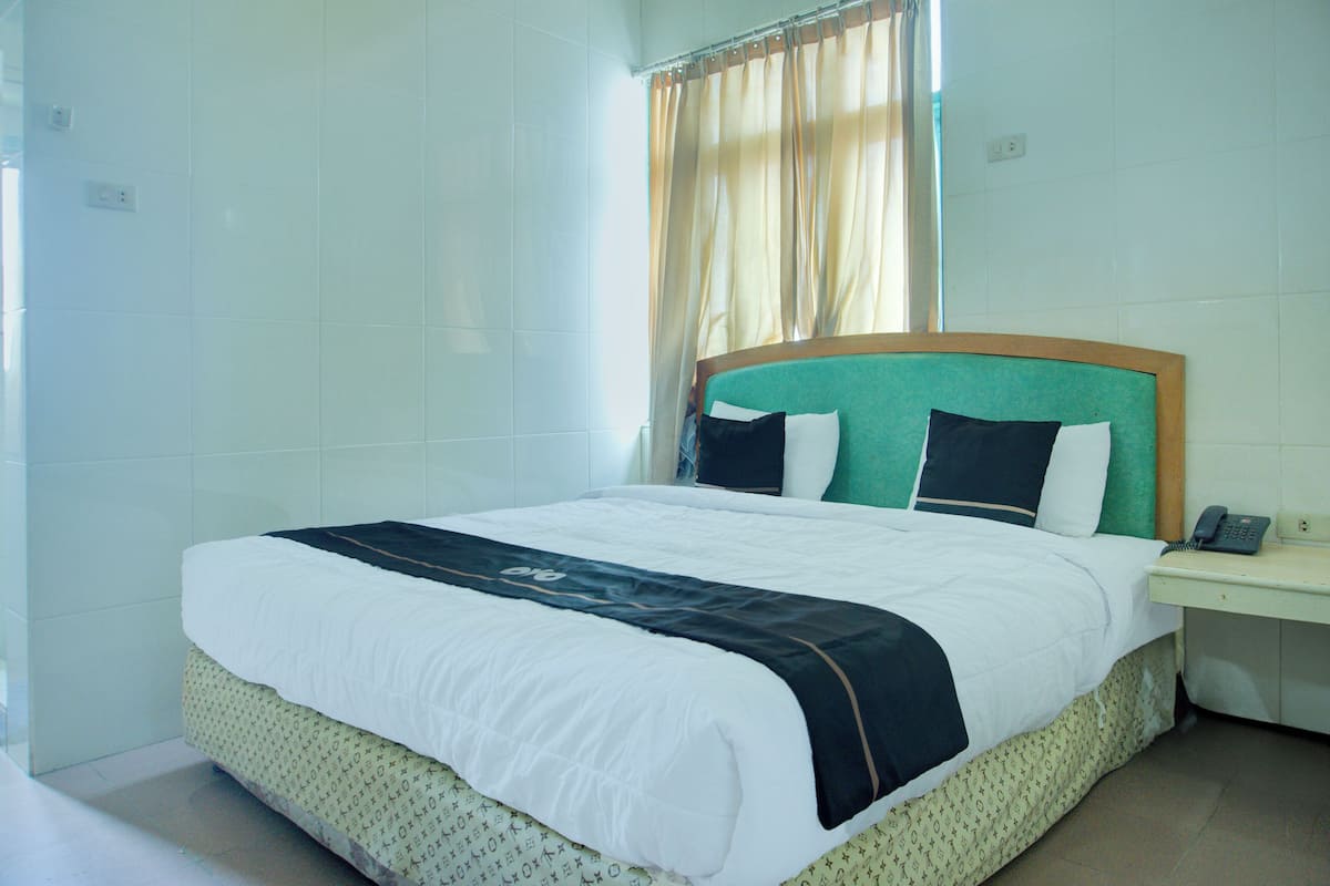 A neatly made bed with a white and black bedspread, a wooden headboard, and a bedside table with a telephone.