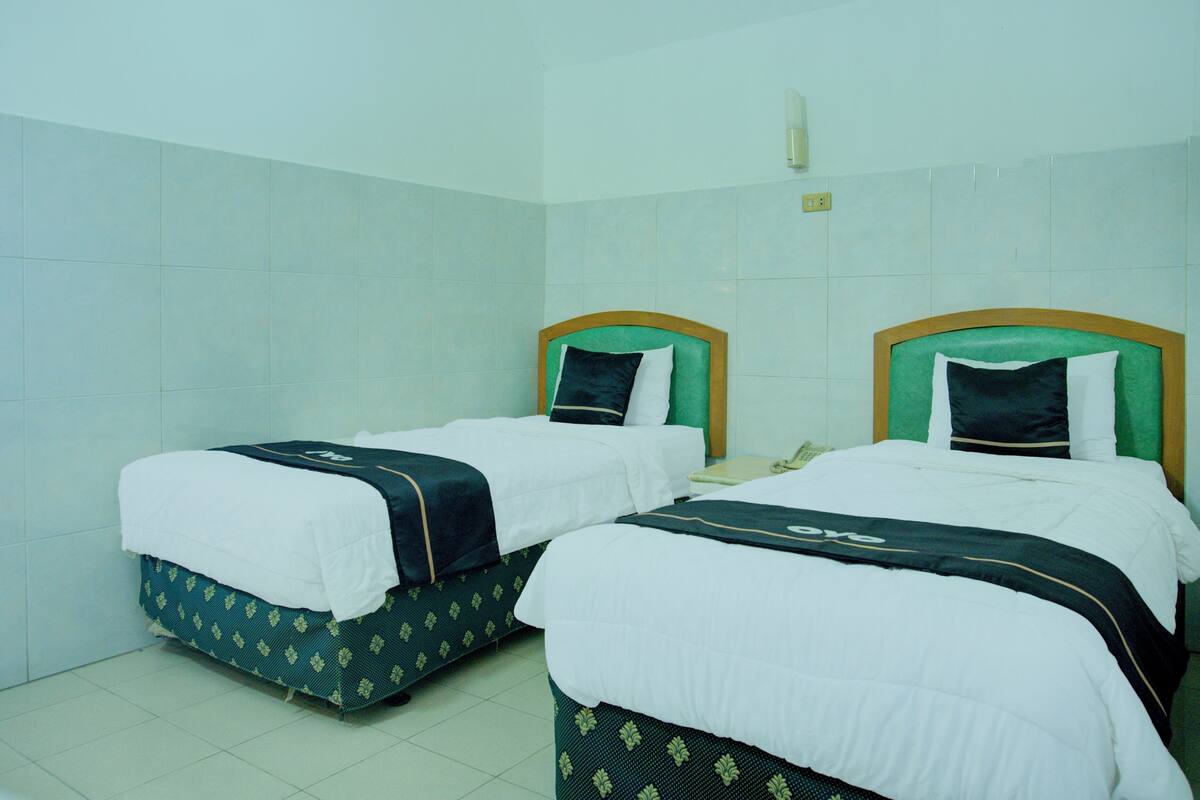 Two single beds with green headboards and white bedding in a room with white tiled walls.