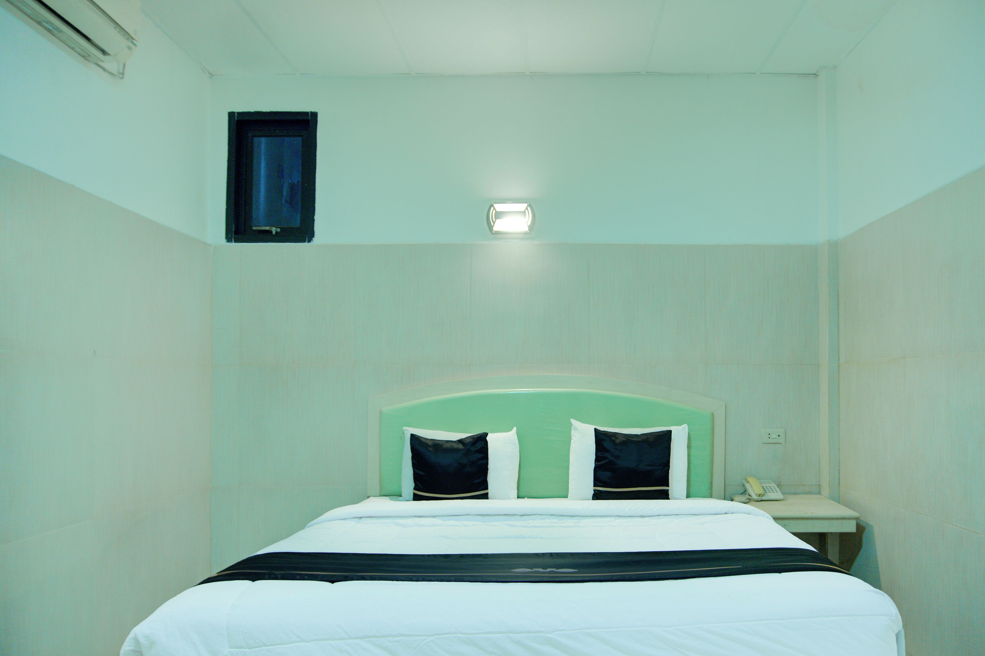 Habitación de hotel con cama, mesita de noche, teléfono y lámpara fijada a la pared.
