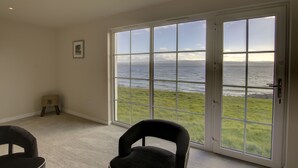 Ein Zimmer mit einer großen SchiebeglasTür, die zu einer grünen Fläche mit Meerblick führt.
