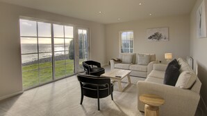 Ein geräumiges Wohnzimmer mit einer großen Schiebeglasdoor zum Balkon, ein beiges Sofa, ein schwarzer Sessel und ein Holztisch.