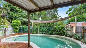 Une piscine avec une terrasse en bois et un hamac.